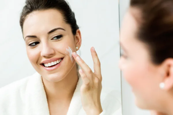 Young woman caring of her skin standing near mirror in the bathr — Stock Photo, Image