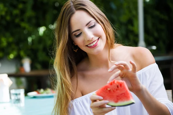 Schöne junge Frau isst Wassermelone im heimischen Garten. — Stockfoto