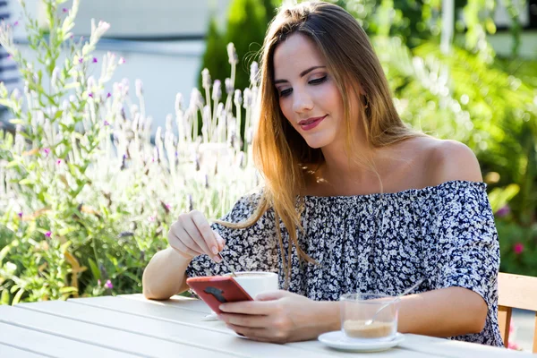 Mooie jonge vrouw met behulp van haar mobiele telefoon in de tuin. — Stockfoto
