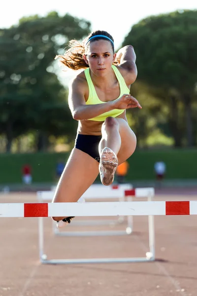 Young athlete jumping over a hurdle during training on race trac — Stock Photo, Image
