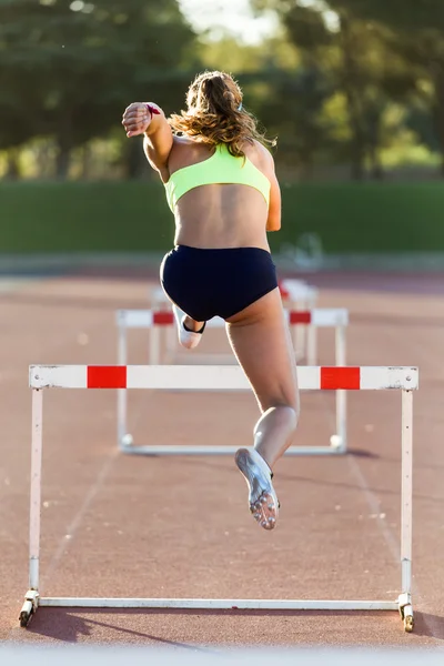Young athlete jumping over a hurdle during training on race trac — Stock Photo, Image