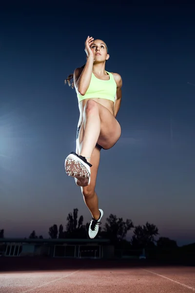 Fit young woman running on track field at night. — Stock Photo, Image