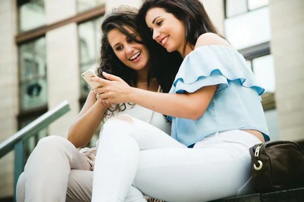 Beautiful young women having fun with smartphones in the street. — Stock Photo, Image