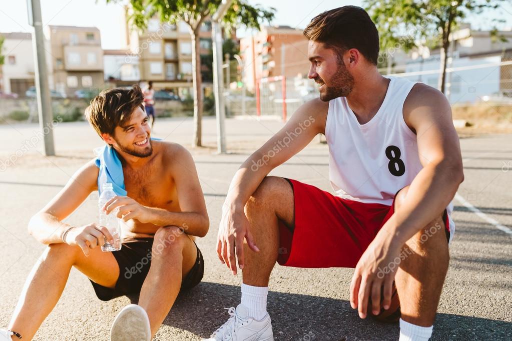 Portrait of two friends relaxing after playing basketball on court.