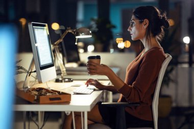 Ofiste kahve içerken bilgisayarla çalışan genç ve güzel bir iş kadınının fotoğrafı..