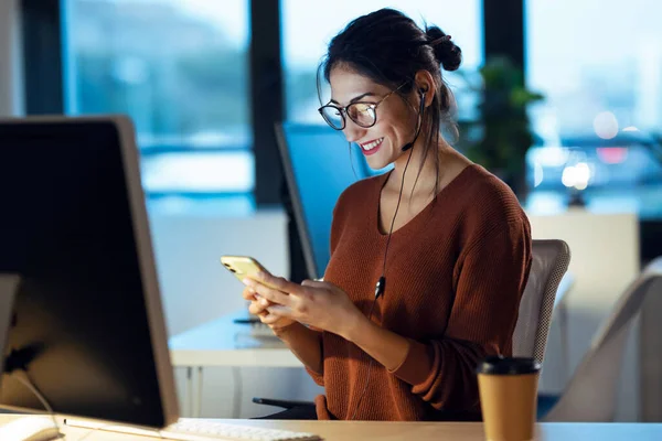 オフィスに座ってコンピュータと仕事をしながら携帯電話でビデオ通話を持っている美しい若いビジネス女性のショット — ストック写真