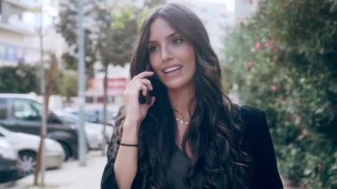 Sokakta yürürken cep telefonuyla konuşan ve gülen genç iş kadınının videosu..