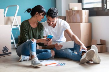 Zeminde oturan akıllı telefondaki yeni daireyi dekore etmek için fikir arayan şirin bir çift fotoğrafı.. 