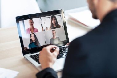 Genç bir erkek çalışanın, çeşitli meslektaşlarıyla evdeki bilgisayarla online brifingde konuştuğu görüntüler..