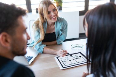 Ofisteki evi satın almak için çiftle konuşurken elektronik tablette ev planları gösteren güzel bir emlakçı fotoğrafı..