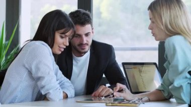 Güzel bir emlakçının, ofisteki evi satın almak için çiftle konuşurken elektronik tablette ev planlarını gösteren videosu..