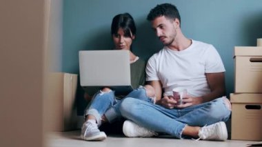 Evde yerde otururken dizüstü bilgisayarla dekorasyon fikirleri arayan çekici genç çiftin videosu..