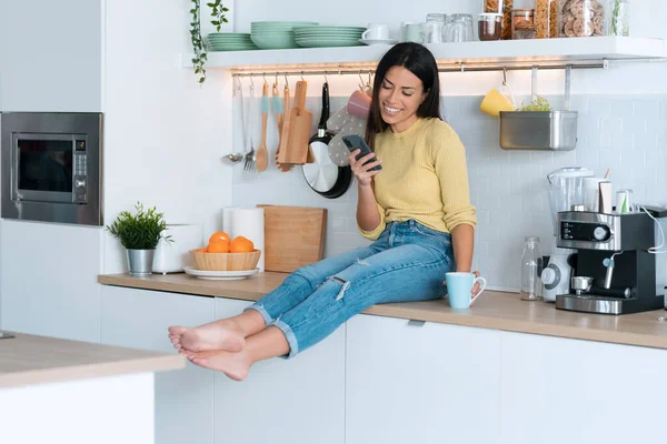 Çekici Genç Bir Kadının Evde Oturup Kahve Içerken Akıllı Telefon — Stok fotoğraf