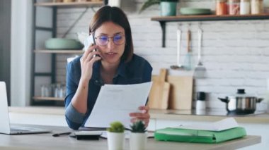 Evdeki mutfakta bilgisayarla çalışırken cep telefonuyla konuşan genç ve güzel bir iş kadınının videosu..