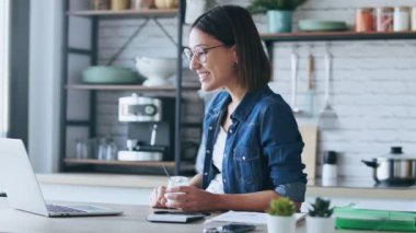 Evde yoğurt yerken dizüstü bilgisayarında sallanan gülümseyen genç bir kadının videosu..