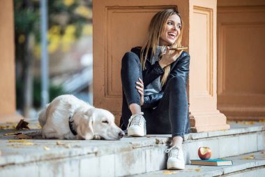 Güzel Golden Retriever köpeğiyle sonbaharda parkta otururken akıllı telefonuyla sesli mesajlar gönderen genç bir kadının fotoğrafı..