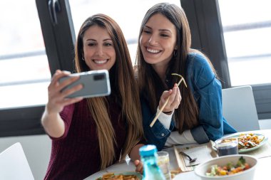 Gülümseyen iki güzel kadının Japon yemeği yerken evdeki mutfakta akıllı bir telefonla selfie çekmesi..