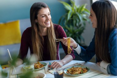 Gülümseyen iki güzel kadının Japon yemeklerini yerken evdeki mutfakta birbirlerine bakmaları..
