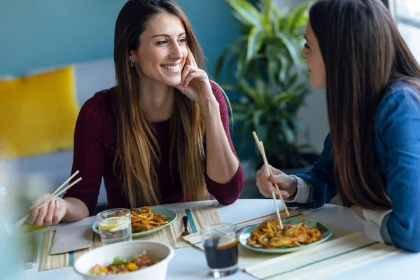 2人の笑顔の美しい女性の友人のショット自宅でキッチンでお互いを見ながら日本料理を食べる — ストック写真