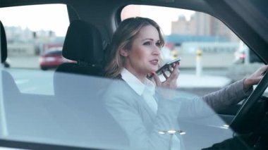 Güzel olgun bir kadının şehir için arabasını sürerken akıllı telefonunu kullanmasının videosu..