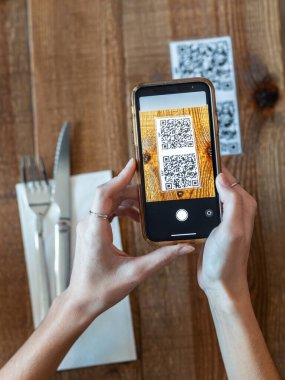 Lokantadaki yemek menüsünü seçmek için QR kodunu taramak için akıllı telefonu kullanan genç kadın ellerini kapat.. 