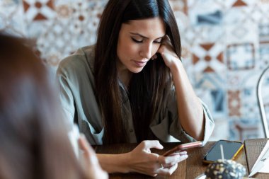 Lokantada arkadaşlarıyla yemek yerken akıllı telefonuyla mesaj gönderen güzel bir kadının fotoğrafı..