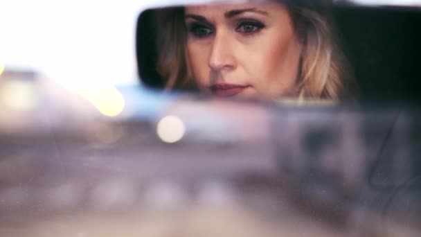 都市で彼女の車を運転しながら車のバックミラーに反映された美しい成熟した女性のバックビューのビデオ — ストック動画