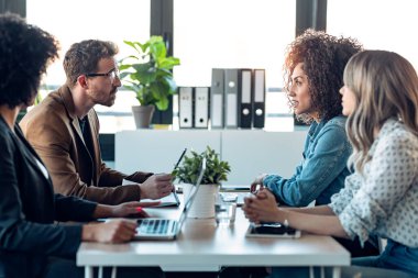 Ofiste yeni projelerinden bahsederken dizüstü bilgisayarlarla çalışan çok yönlü iş adamlarının fotoğrafları..