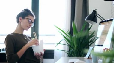 Yemek çubuklarıyla erişte yiyen mutlu genç bir kadının videosu. Evde, ofiste bir sandalyede otururken..