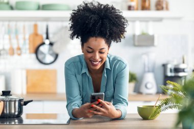 Evdeki mutfakta çubuklarla erişte yerken akıllı telefonuyla mesaj gönderen güzel afro bir kadın..