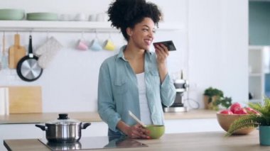 Evde yemek çubuklarıyla erişte yerken cep telefonuyla ses gönderen gülümseyen Afro kadının videosu..