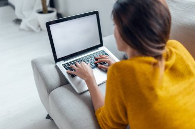 Evdeki kanepede yatarken dizüstü bilgisayarıyla çalışan güzel bir kadının fotoğrafı..