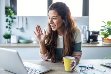 Evde yoğurt yerken dizüstü bilgisayarın kamerasından gülümseyen genç bir kadının fotoğrafı..