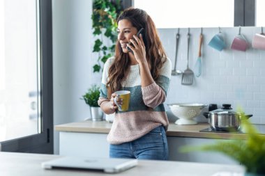Evdeki mutfakta bir fincan kahve içerken genç ve güzel bir kadının cep telefonunu kullanması..