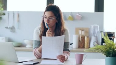 Evdeki mutfakta donut yerken dizüstü bilgisayarından gülümseyen genç bir kadının videosu..
