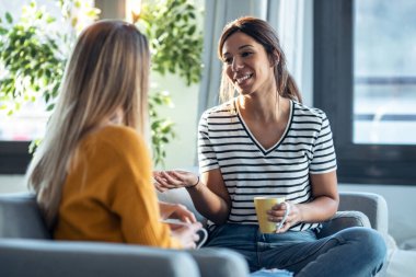 Oturma odasındaki kanepede oturmuş akıllı telefon izlerken gülümseyen iki genç kadının görüntüsü..