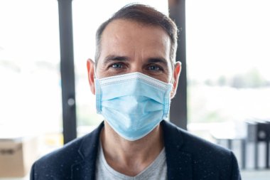 Ofisteki kameraya bakarken başkalarının virüsü görmesini engellemek için hijyenik maske takan olgun yakışıklı bir adamın portresi..