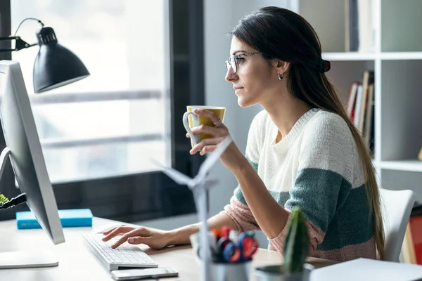 現代のスタートアップオフィスでコーヒーを飲みながらコンピュータで働く濃縮若いビジネス女性のショット — ストック写真