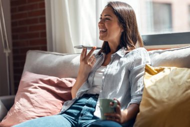 Evdeki kanepede oturan güzel, gülümseyen bir kadının cep telefonu kullanması..