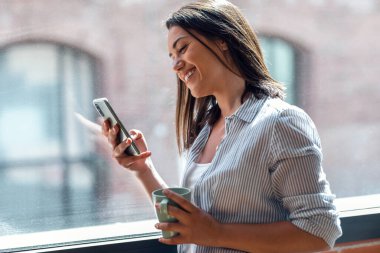 Evdeki pencerenin yanında duran güzel genç bir kadının cep telefonunu kullanması..