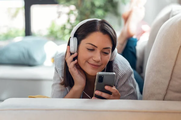 Strzał Uśmiechniętej Młodej Kobiety Słuchającej Muzyki Pomocą Smartfona Siedząc Kanapie — Zdjęcie stockowe