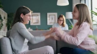 Evdeki oturma odasında kanepede oturmuş el ele oyun oynayan iki kız kardeşin videosu..