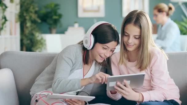 两个可爱的姐姐在家里的客厅里用数码平板电脑和她的妈妈一起工作的视频 — 图库视频影像