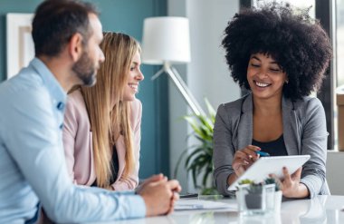 Ofisteki evi satın almak için çiftle konuşurken elektronik tablette ev planları gösteren güzel bir emlakçı fotoğrafı..