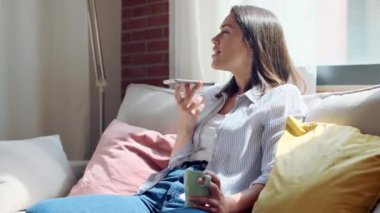 Evdeki kanepede oturan, cep telefonu kullanan güzel, genç bir kadının videosu..