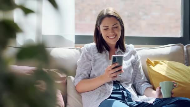 Video Vackra Unga Leende Kvinna Med Mobiltelefon Sitter Soffa Hemma — Stockvideo