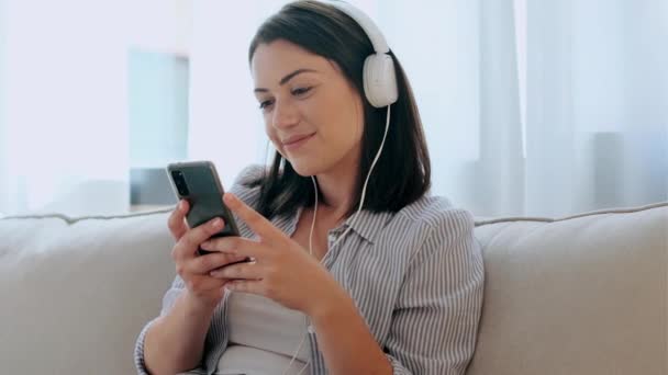 Vídeo Uma Jovem Sorridente Ouvindo Música Com Smartphone Enquanto Senta — Vídeo de Stock