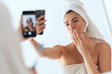 Evdeki banyoda selfie çekerken dişlerini fırçalayan güzel bir genç kadın..