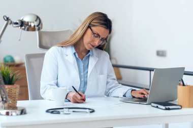 Konsültasyonda bilgisayarla çalışan olgun, konsantre ve çekici bir kadın doktor..