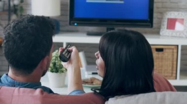 Evdeki kanepede televizyon seyrederken uzaktan kumandayla kanal değiştiren rahat genç çiftin videosu..